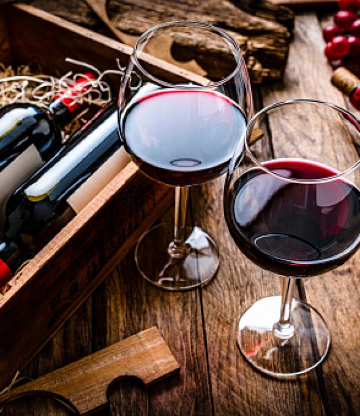 High angle view of two red wineglasses shot on rustic wooden table.  A box with two new wine bottles, straw, a corkscrew with a cork and grapes complete the composition. Predominant colors are red and brown. High resolution 42Mp studio digital capture taken with SONY A7rII and Zeiss Batis 40mm F2.0 CF lens